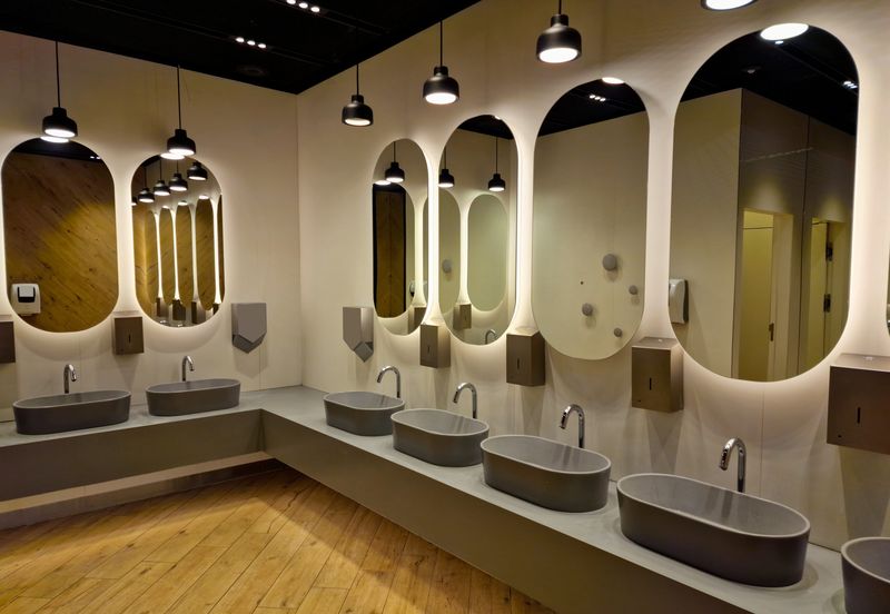 Commercial restroom with a long counter of vessel sinks, touchless faucets and backlit oval mirrors