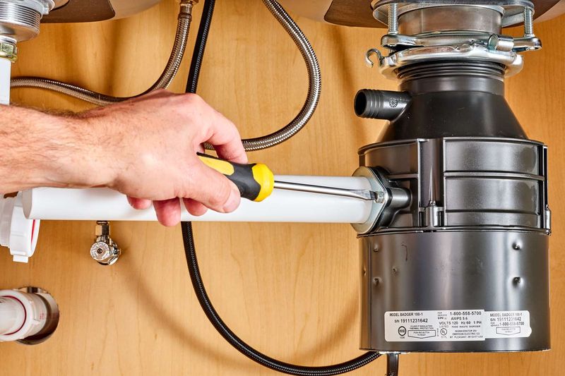 A hand tightening a garbage disposal under a sink with a screwdriver
