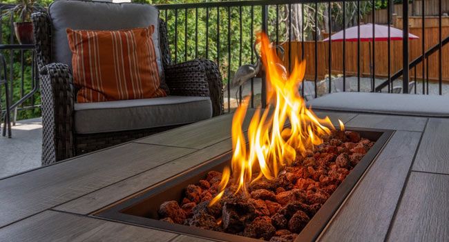 Flames rising from the lava rock of a gas fire pit table on a patio