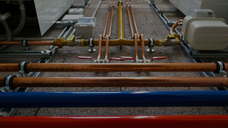 Parallel copper water lines and a yellow gas header with red-handled shut-off valves on strut supports