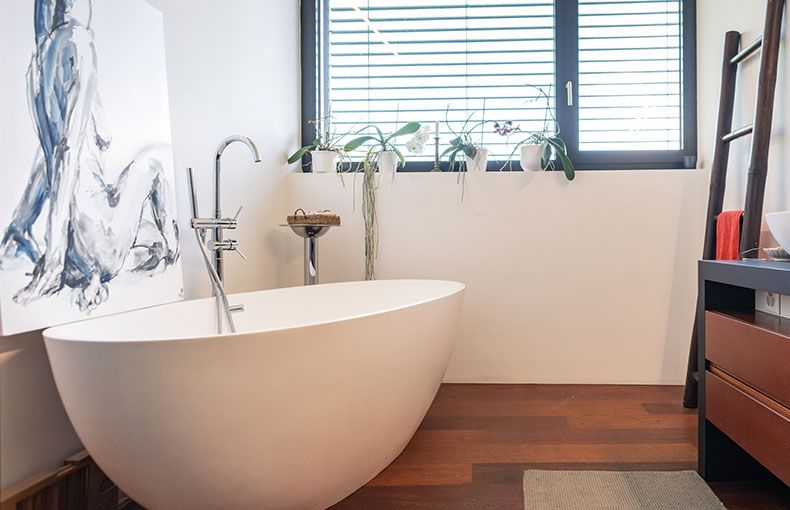 Bright bathroom with a white freestanding tub, a floor-mounted tub filler and wood floors
